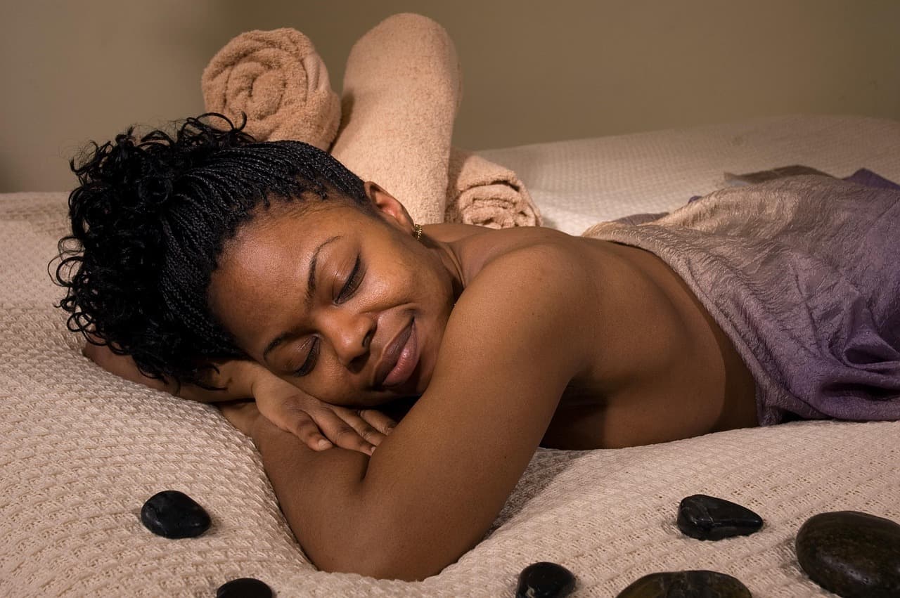 A woman resting on a treatment bed with warm stones beside her