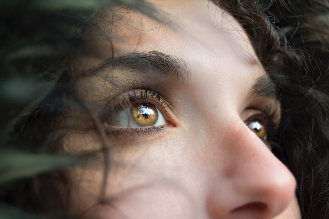 Close-up of a woman with dark, defined brows and hazel eyes, looking up